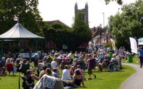 Crowd of people in park, with bandstand and gazebos.