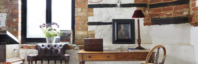 white and red brick wall, oak furniture, chair to the left, flowers, lamp, and picture in background.