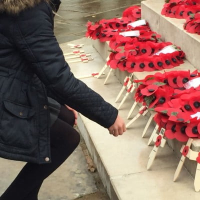 Girl lays wooden cross on war memorial.