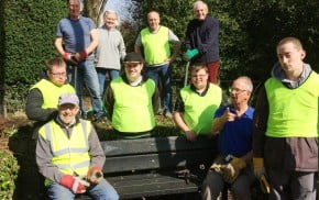 Nine males and one female sitting on a bench or standing behind wearing hi res clothing and gardening gloves