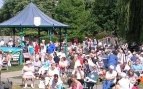 Crowd of people in park. Bandstand behind.