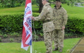 Two males attaching flag to flag pole in park.