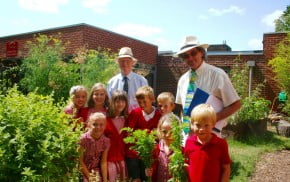 Two males with a group of school children in a garden.