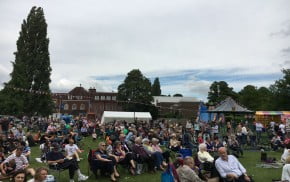 Groups of people sitting on chairs in the park watching a band.