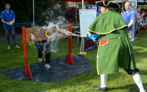 Male in stocks while male throws an bucket of water at him