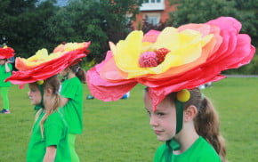 Children performers with green costumes and large flower hats .