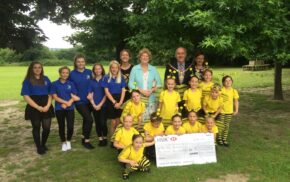 A group of adults and children with a large cheque stood in a park.