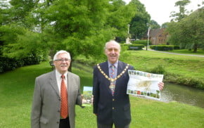 Two males holding a leaflet in a park.