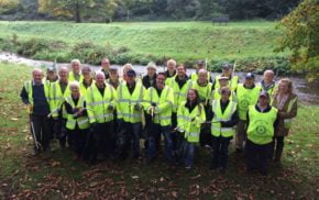 Group of people in high viz jackets with litter pickers and black sacks.