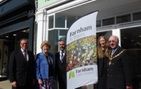 Five people standing with Farnham in Bloom sail flag outside Specsavers shop.