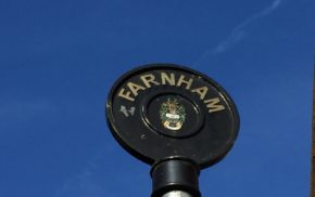 Rounded top of black iron sign post with Farnham painted in gold lettering.