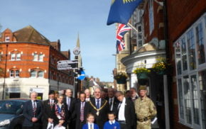 A group of people including soldiers, the Mayor and two children stand beneath Commonwealth flag.