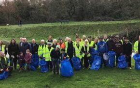 Group of people wearing high viz jackets and standing on grassy area holding blue sacks and litter pickers.