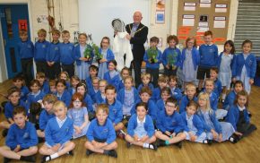 50+ school children sitting and standing in a group. Mayor holding bee keeper's suit.