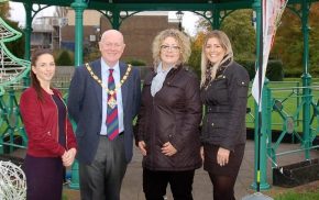 Mayor and three females in front of bandstand decorated with Christmas decorations.