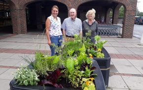 3 people standing behind two planters filled with vegetables ripe for harvest.