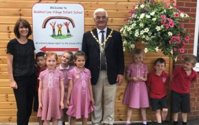 School children and the Mayor stand next to a large hanging basket.