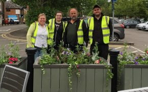 Four people standing behind a flower planter.