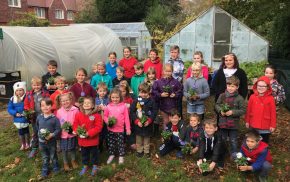 Children standing in front of an allotment holding potted plants.