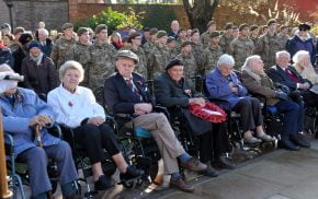 Older people in wheelchairs and soldiers standing behind.