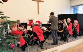 Brass band sitting on a stage wearing Christmas hats.