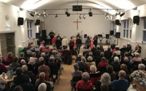 Older people watching a band perform inside a church hall