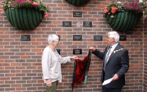 Mayor and female remove a drape to unveil a plaque on a wall.