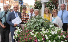 Group of people standing behind a hop cart filled with flowers.