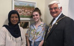 Two females and man stand in front of a painting of poppies.