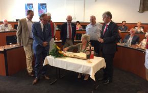 Mayor signs a book in a formal meeting room watched by a group of observers