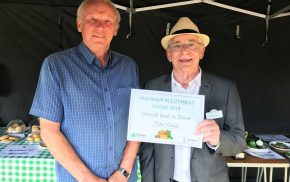 Two men in a marquee. Man on right presents a certificate.