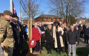 Group of people standing in semi circle. Trees and union flag in background