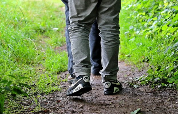 Trousered legs of two people walking in tandem along a footpath