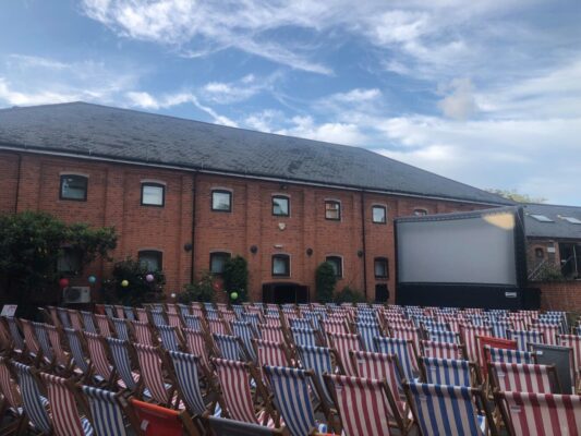 A photo of the Farnham Maltings - Outdoor Cinema set up with a big screen and rows of deckchairs