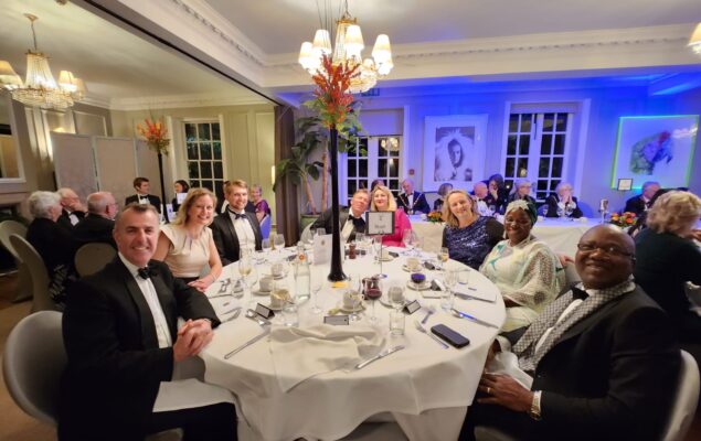 People at a black tie dinner. Sitting at a round table laid with white cloths.