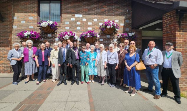 Group of people standing in front of a brick wall displaying commemorative plaques.