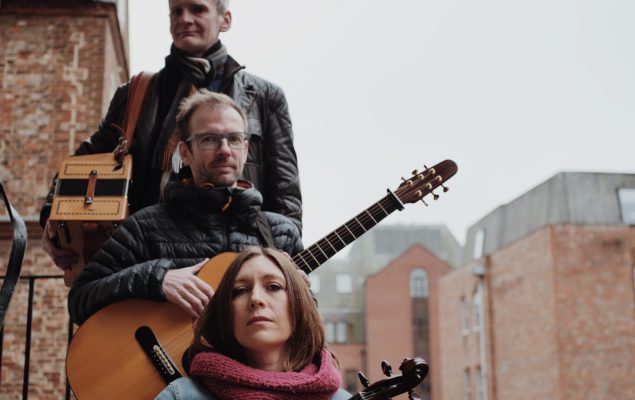 three band members holding instruments stood on stairs