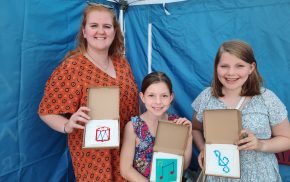 Woman and two girls showing a cross stitch sample.