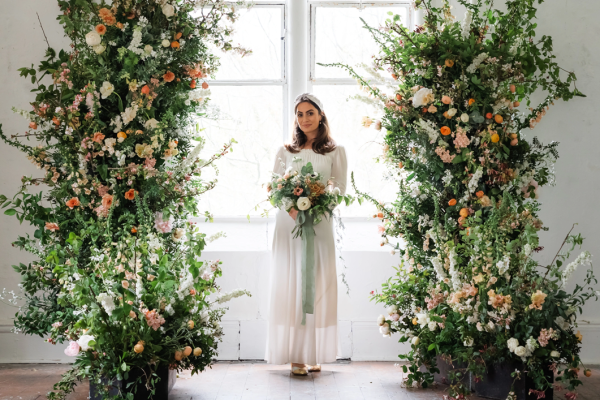 Photo of a bride under a floral arch, holding a bouquet of flowers