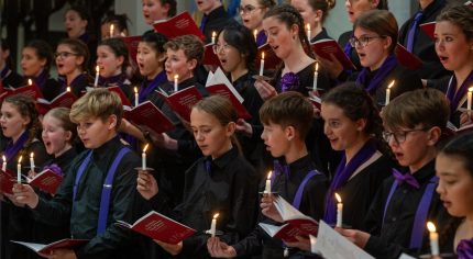 Young people singing by candlelight in a choir.