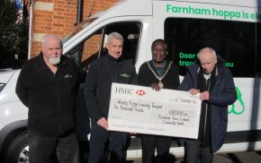 Four men standing in front of a bus holding a large cheque.