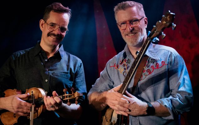 Two men smiling at the camera holding musical instruments