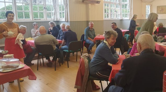 Picture of groups of people talking sat around circular tables in a village hall