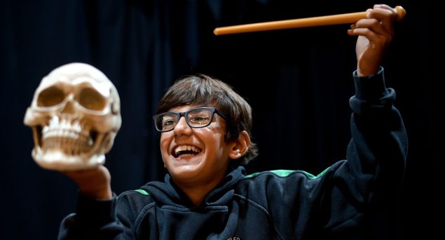 Picture of a boy with glasses smiling and holding a skull mask