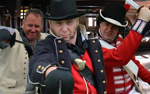Three men dressed in 18th century naval uniforms